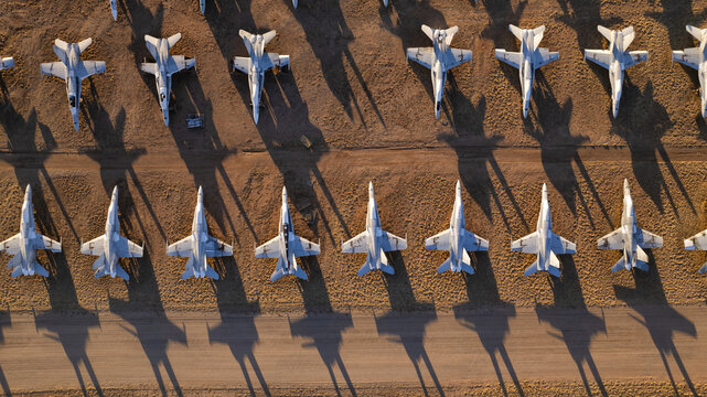 Tucson, United States - 06 February 2025: Aerial view of silver-grey fighter jets casting long, stark shadows across the warm, ochre desert floor.
