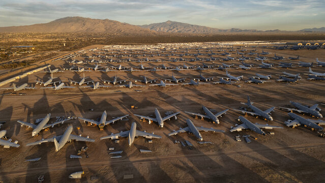 Tucson, United States - 30 January 2025: Aerial view of a boneyard of retired military aircraft on the desert floor, with mountains under a golden sky.