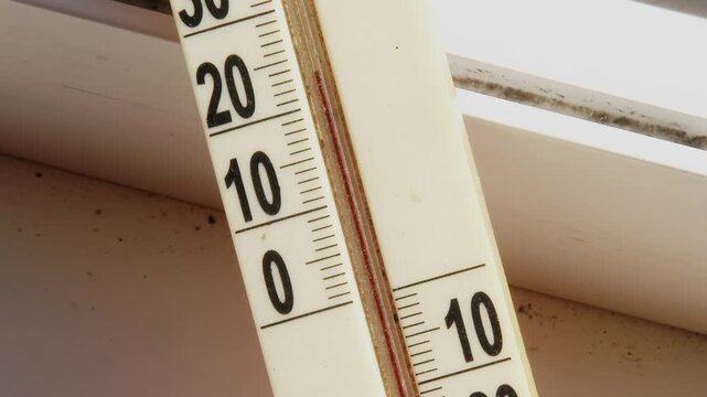 Close up of dusty outdoor thermometer on window with rising mercury on sunny day.