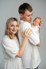 Fototapeta premium mother and father with a baby in their arms, a young family holding a newborn baby, gently hugging and kissing it on a white background, space for text, a happy family