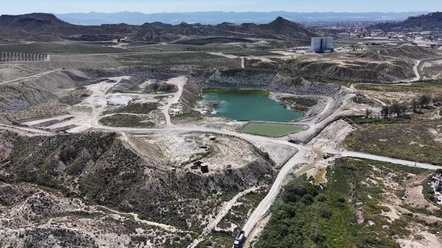 A tracking drone shot of a limestone quarry featuring a green water deposit and industrial infrastructure nestled in the arid hills of Murcia.