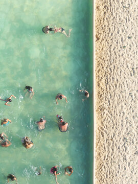 Figueira da Foz, Portugal - 08 August 2024: Aerial view of swimmers enjoying the cool, translucent water contrasting with the warm, textured sand.