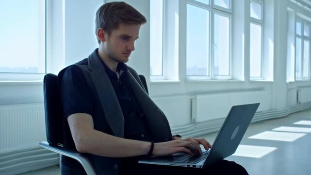 Static shot of young man typing on laptop in bright office interior near large windows side view contemplative posture with digital glitch distortion across scene