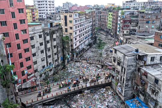 Keraniganj, Bangladesh - 11 April 2026: Aerial view of a dense urban sprawl where varied buildings frame a vast, choked waterway of refuse, traversed by a bustling bridge.