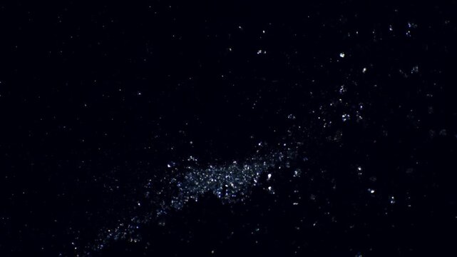 Slow motion tracking shot of glitter particles scattering and drifting across black studio background close up micro detail