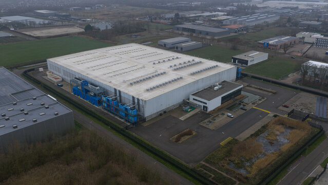 Aerial view of a large, white warehouse with blue shipping containers and a modern office building, reflecting the industrial heart of the region, Roosendaal, North Brabant, Netherlands.