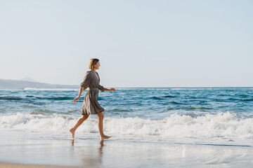 Obraz premium Happy woman runs and jumps by the ocean. Concept freedom and carefree vacation. Beach Holidays. Carefree woman splashing water having fun on the beach. Young girl enjoying fresh air on ocean shore.