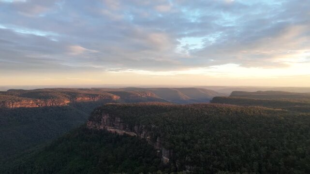 Low altitude aerial drone reveal shot of a deep forested canyon in Bundanoon, Southern Highlands, New South Wales, Australia. Moody blue sky and clouds above dark eucalyptus covered valley.