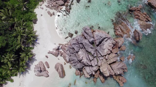 Bird eye drone view of granites stones near shoreline, clear turquoise water, white sandy beach, people snorkelling, coconut palm trees near the beach, anse cocos, La Digue, Seychelles 008.