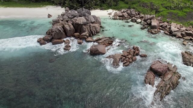 Push back drone view of granites stones near shoreline, clear turquoise water, people snorkelling, white sandy beach, anse cocos, La Digue, Seychelles 011