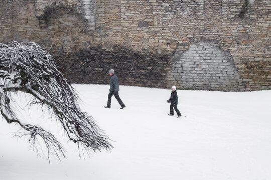 Tallinn, Estonia - 03 January 2025: View of people traversing the snow-covered grounds near the imposing stone walls, a stark contrast of cold stone and the soft, enveloping snow.