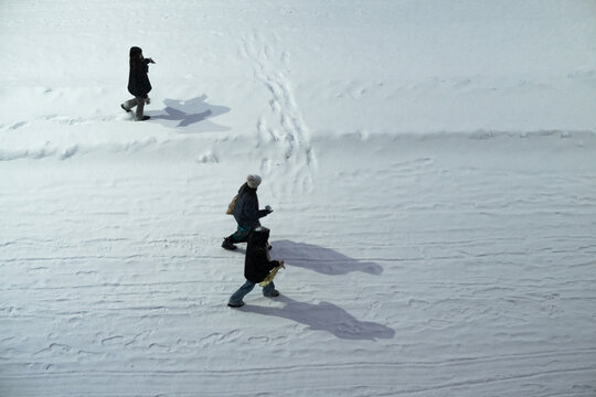 Tallinn, Estonia - 03 January 2025: View of three figures traversing a pristine, snow-covered landscape, casting long, dark shadows across the brilliant white expanse.
