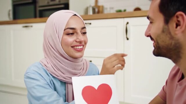Muslim woman holding heart card and touching husband's nose