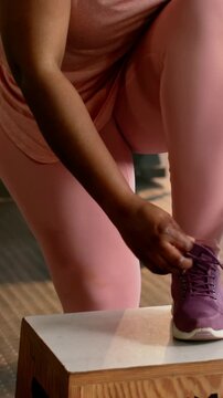 Vertical video: Lifting foot onto plyo box, pink-clad woman securing purple shoe at gym for workout