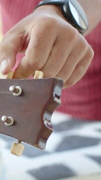 Vertical video: Starting above pegs, right hand tuning uke for playing at home, red top and watch