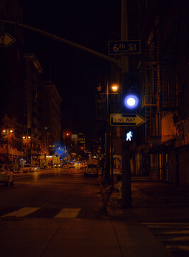 Los Angeles, United States - 29 March 2024: View of a quiet 6th St intersection at night, where a vivid blue pedestrian signal glows amidst warm orange streetlights.