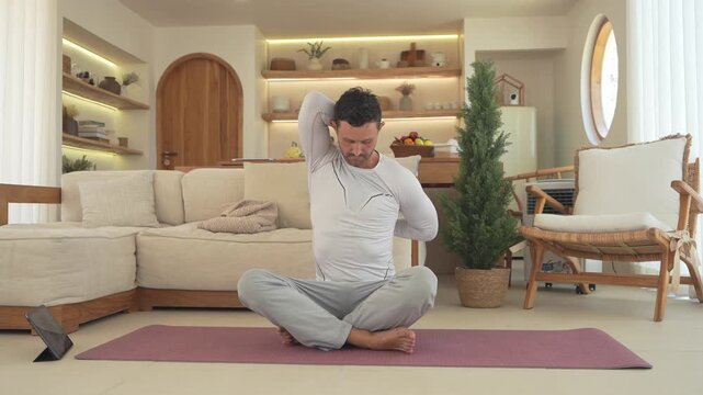 A man performs various yoga stretches and poses while seated on a mat in a beautifully decorated, sunlit living room, demonstrating a mindful practice