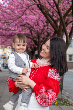 Smiling mother holding toddler under cherry blossom trees Portrait