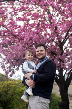 Father holding baby under pink cherry blossoms in spring Vyshyvanka