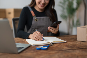 Naklejka premium Woman writing orders checking products on smartphone