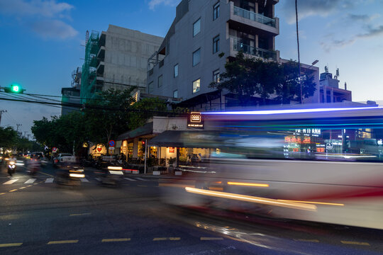 Da Nang, VIETNAM &ndash; 14 November 2025: A bus streaks past a busy intersection in Da Nang, Vietnam, with motorbikes and pedestrians moving about in the evening.
