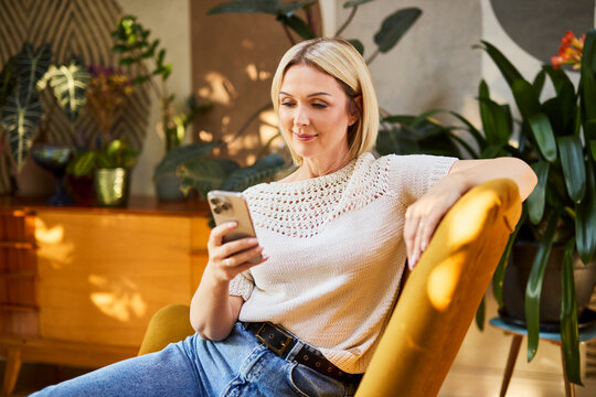 Woman sitting on chair at home using smartphone and relaxing
