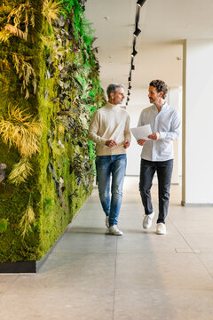 Two men walking and discussing business in a modern office with a green wall