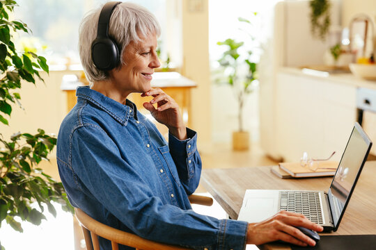 Smiling freelancer sitting with hand on chin using laptop at home office