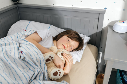 Boy sleeping peacefully in a cozy bed hugging a teddy bear at home