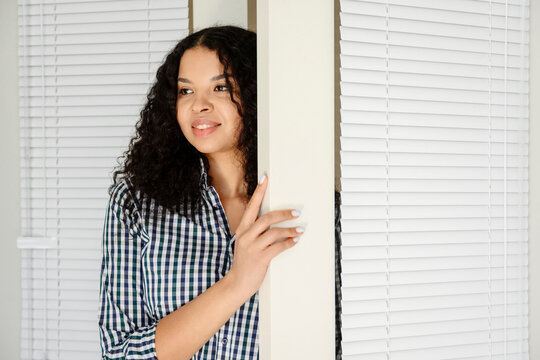 Smiling homeowner peeking through doorway with window blind