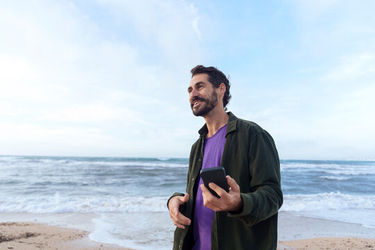 Smiling man standing with mobile phone at beach