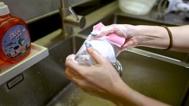 Close Up of Asian Woman Hands Washing Glass Mug in Kitchen Sink