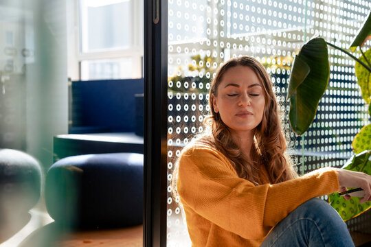 Mature businesswoman leaning with eyes closed on glass in office