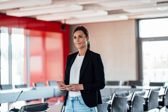 Businesswoman with smart phone standing in conference room at office