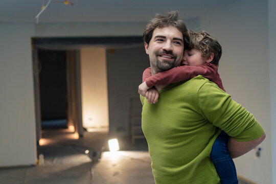 Smiling father piggybacking son and spending leisure time in new apartment