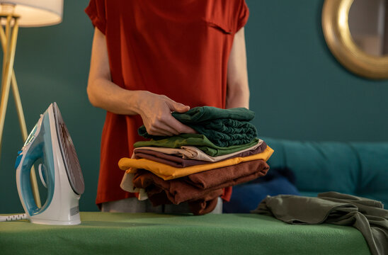 Hands holding folded laundry beside iron indoors at home