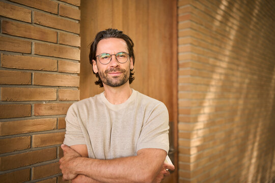 Confident independent man with glasses standing by brick wall