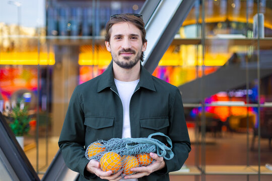 Shopper holding reusable net bag with fresh orange in the city