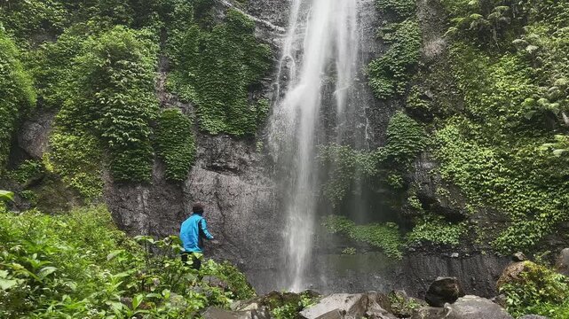 Traveler exploring a powerful waterfall in a vibrant tropical rainforest, capturing breathtaking moments. Ideal for adventure, ecotourism, and nature travel concepts.