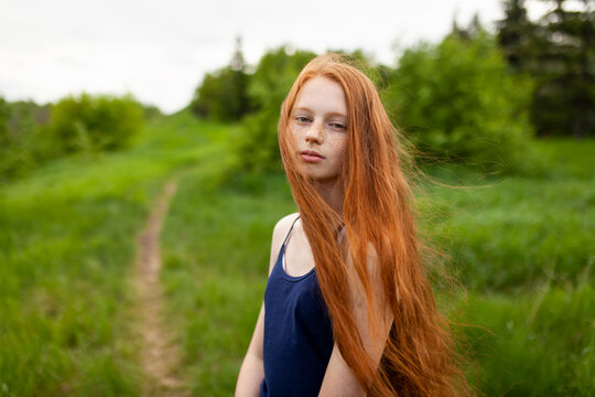 Teenager with red hair and freckles in a green summer meadow