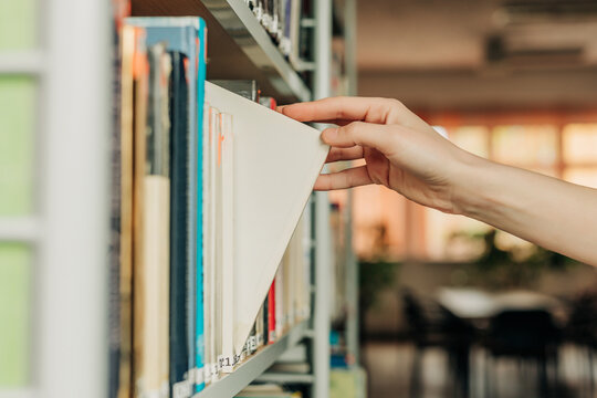 Hand selecting a white book from a library shelf indoors