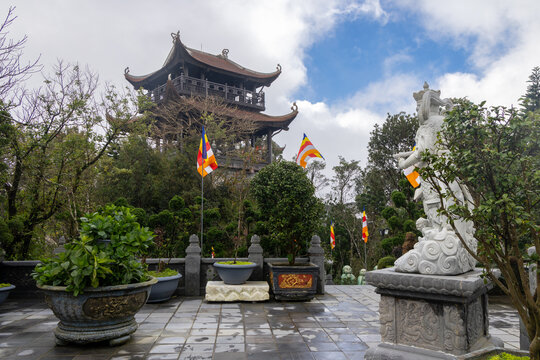 A statue and Buddhist flags adorn the grounds of a Pagoda, a popular destination for tourists and locals in Ba Na Hills, Da Nang, Vietnam.