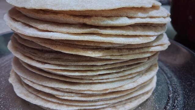 In this picture, fresh, homemade chapatis (rotis) are seen stacked one on top of another on a steel plate. They are round, soft, and feature brown spots.
Fresh chapatis are stacked one atop another on