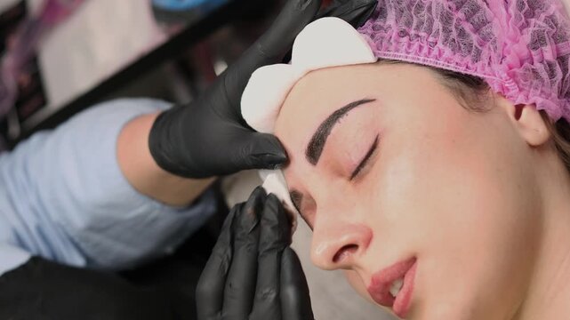 Close up of permanent eyebrow makeup procedure, beautician performing microblading with precision tool in beauty salon