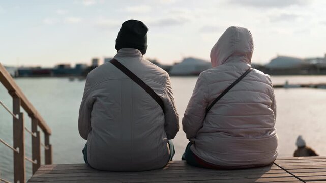 A man and a woman sit in warm clothes and shrivel at sea. The view from the back, without a face.