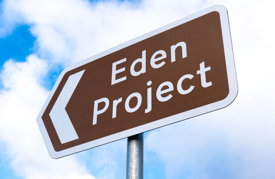 Low angle view of a brown information road sign, with directional arrow reading Eden Project, against a blue sky with white clouds.