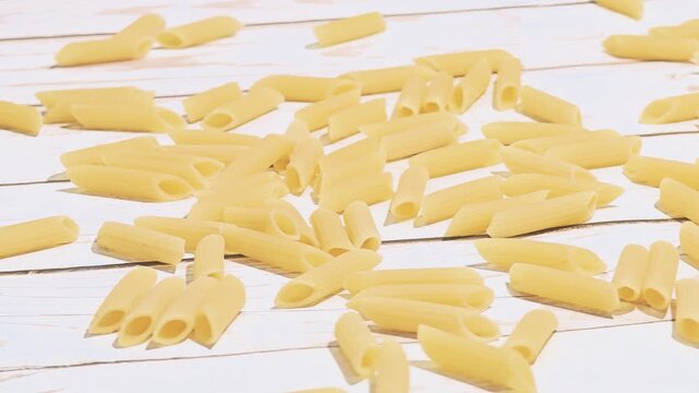 Dried pasta pieces scattered on a wooden surface. Various shapes and sizes of uncooked pasta are visible, showcasing a light yellow color.