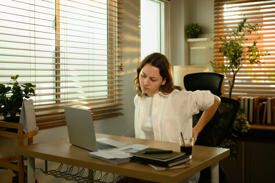 White female office worker holding her back, showing discomfort caused by poor posture and prolonged sitting