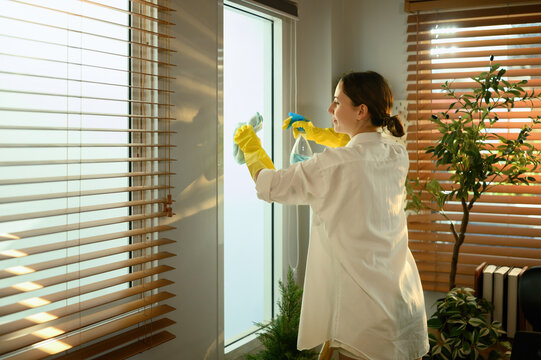 Caucasian woman wiping glass surface and maintaining cleanliness, enjoying a fresh and organized living space