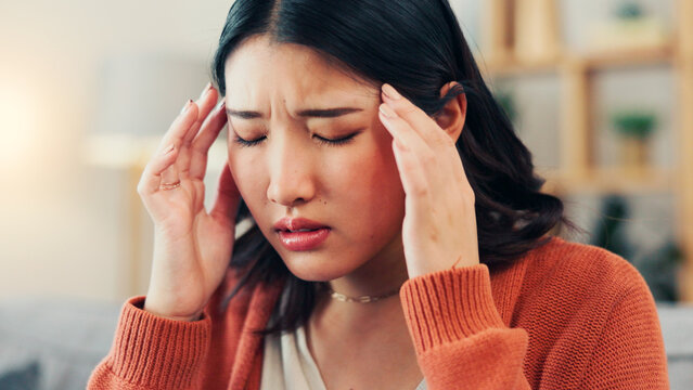 Pain, headache and Asian woman in home with stress for strain, migraine and medical crisis. House, health and upset person with tension, brain fog and massage temples for fatigue and pressure